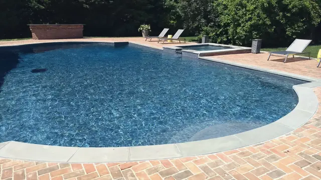 Freeform pool and spa with a herringbone brick patio